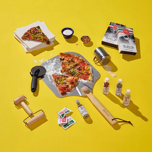 Showcasing ingredients and tools for grilling pizza, including recipe cards and a bottled drink. Items are scattered as if preparing for a pizza party, representing the Chef Dad category in the Father's Day gift guide.